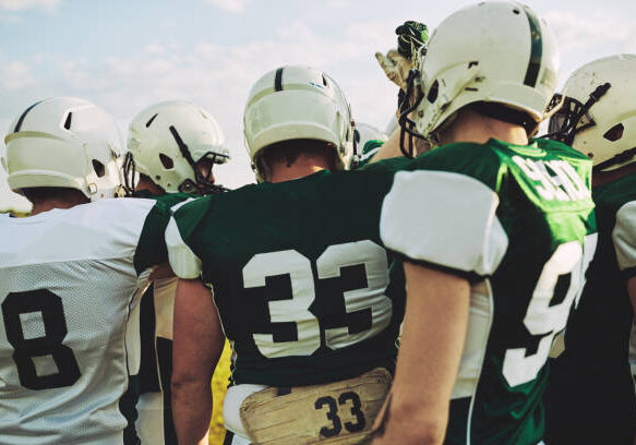 Group of young American football players standing together with their arms raised in a huddle before a game